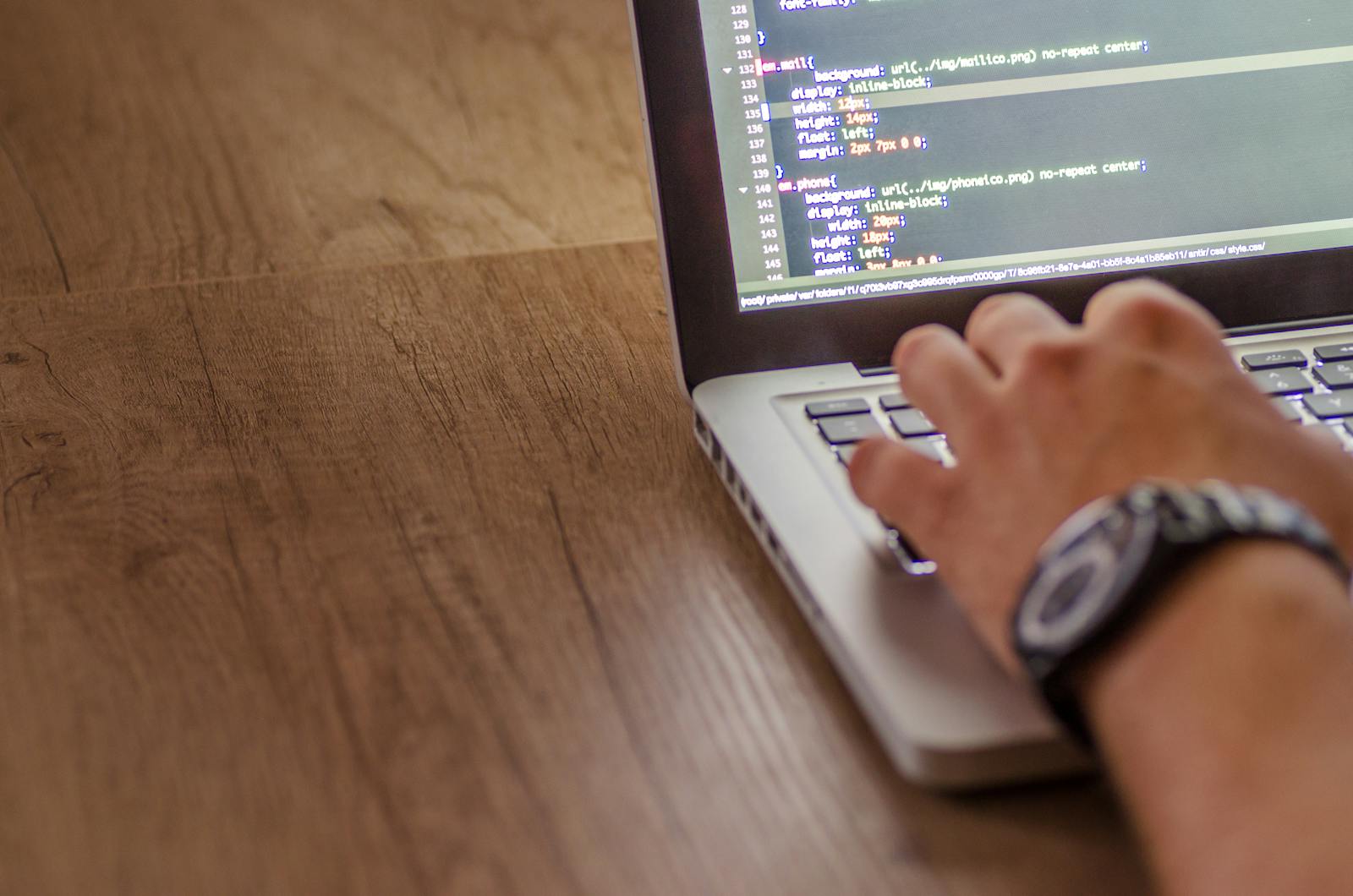 Hands typing CSS code on a MacBook on a wooden desk — photo by goumbik on Pexels