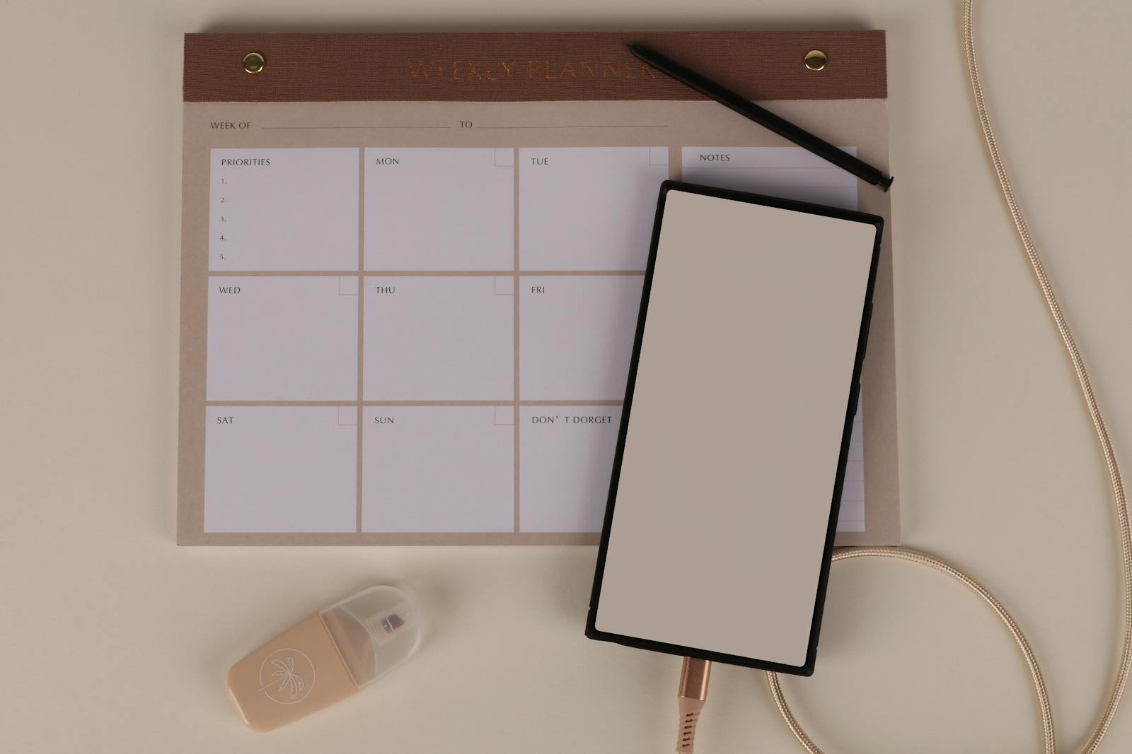 Weekly planner notepad with smartphone, charging cable and pen on a beige desk — photo by ann-h-45017 on Pexels
