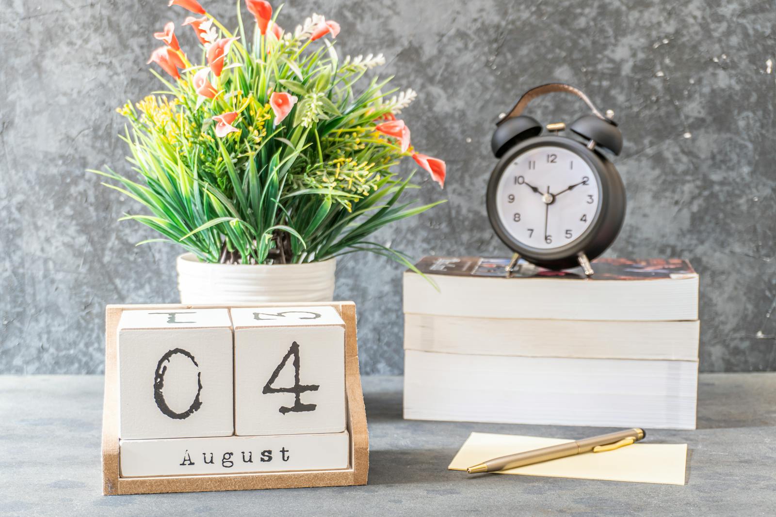 Wooden calendar blocks beside an alarm clock and books — photo by Fauzanfitria on Pexels
