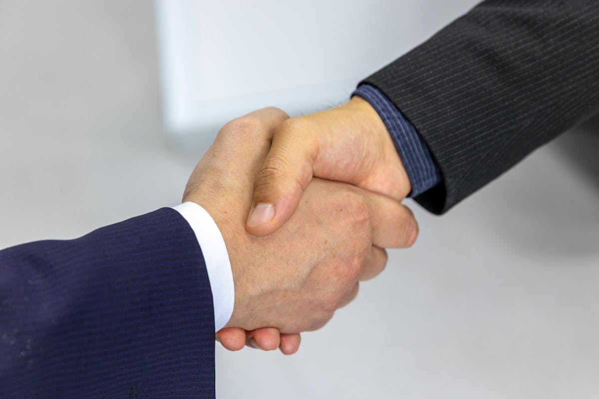 Close-up of two people in business suits shaking hands — corporate partnership/agreement context (photo: Bia Limova / Pexels)