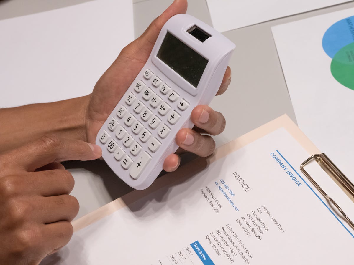 Hands using a calculator next to a printed invoice — usage-based billing context (photo: Kindel Media / Pexels)