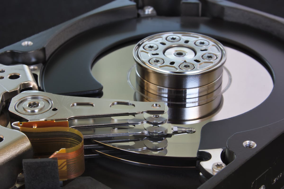 Close-up of an open mechanical hard drive showing the spinning platter and read/write actuator arm — physical-storage context for backup discussion (photo: Amalia Digital / Pexels)