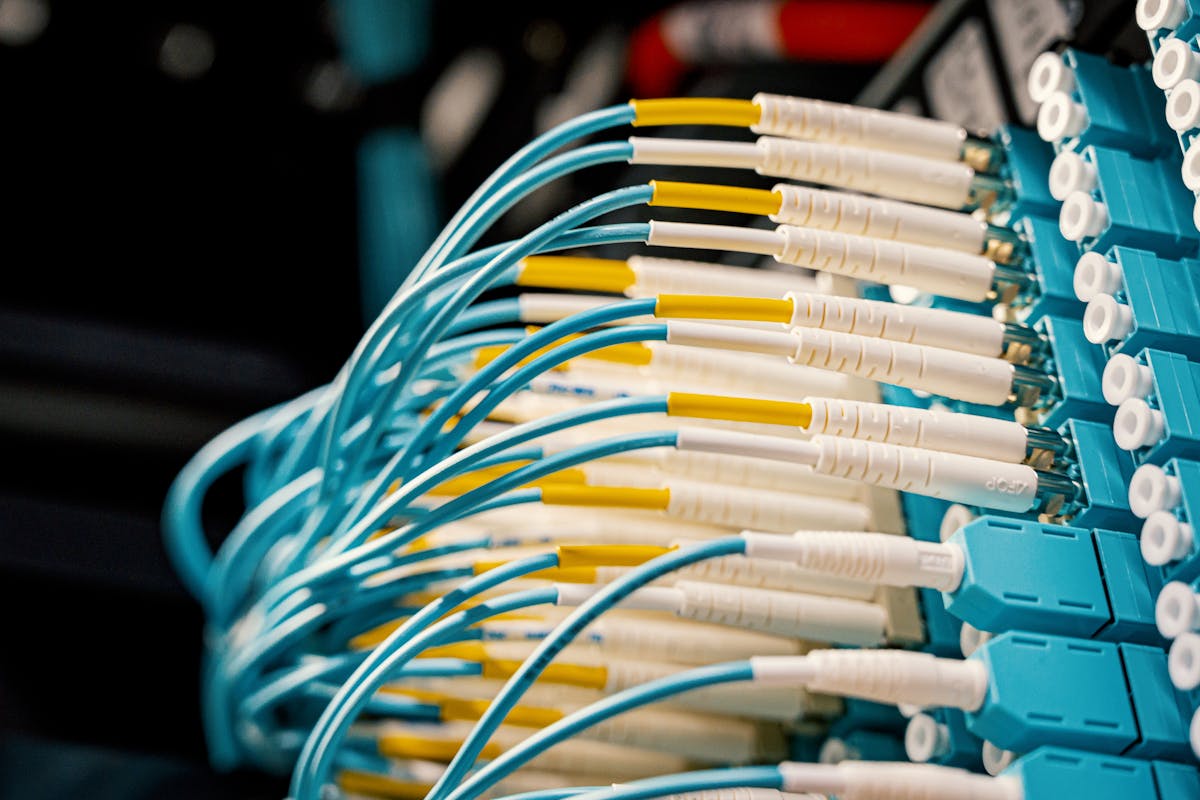 Close-up of fiber optic patch panel with yellow and white connectors plugging into blue ports — visual metaphor for ProxyJump tunneling traffic through one server to reach another (photo: Brett Sayles / Pexels)