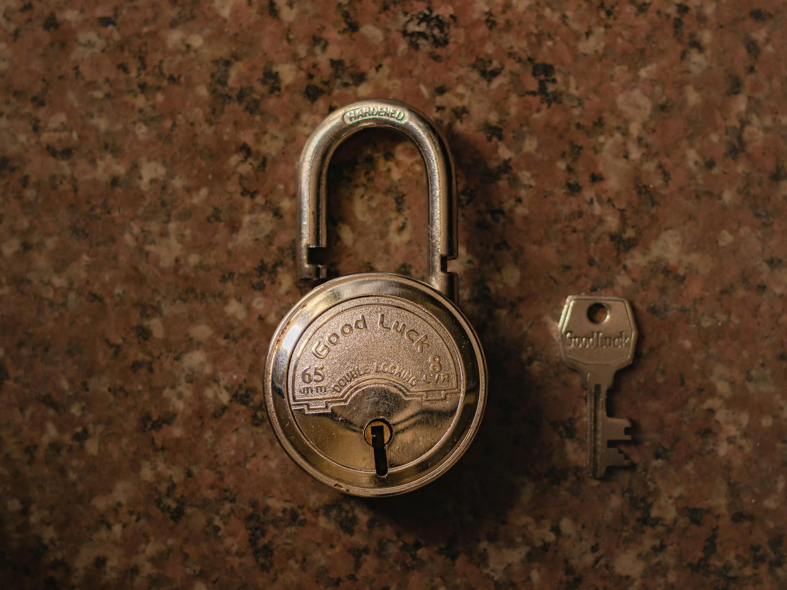 Brass padlock and matching key on a granite surface — photo by theshantanukr on Pexels