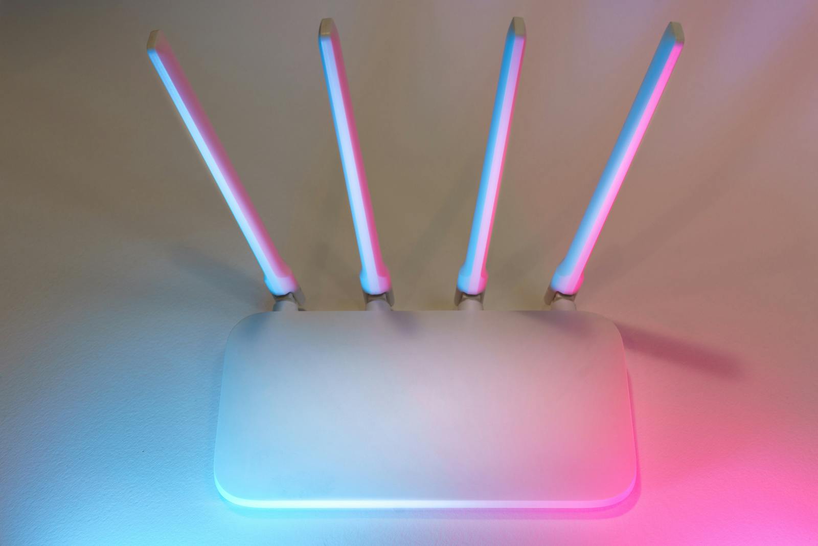 Wi-Fi router with four antennas glowing pink and blue against a wall — photo by Jakub Zerdzicki on Pexels