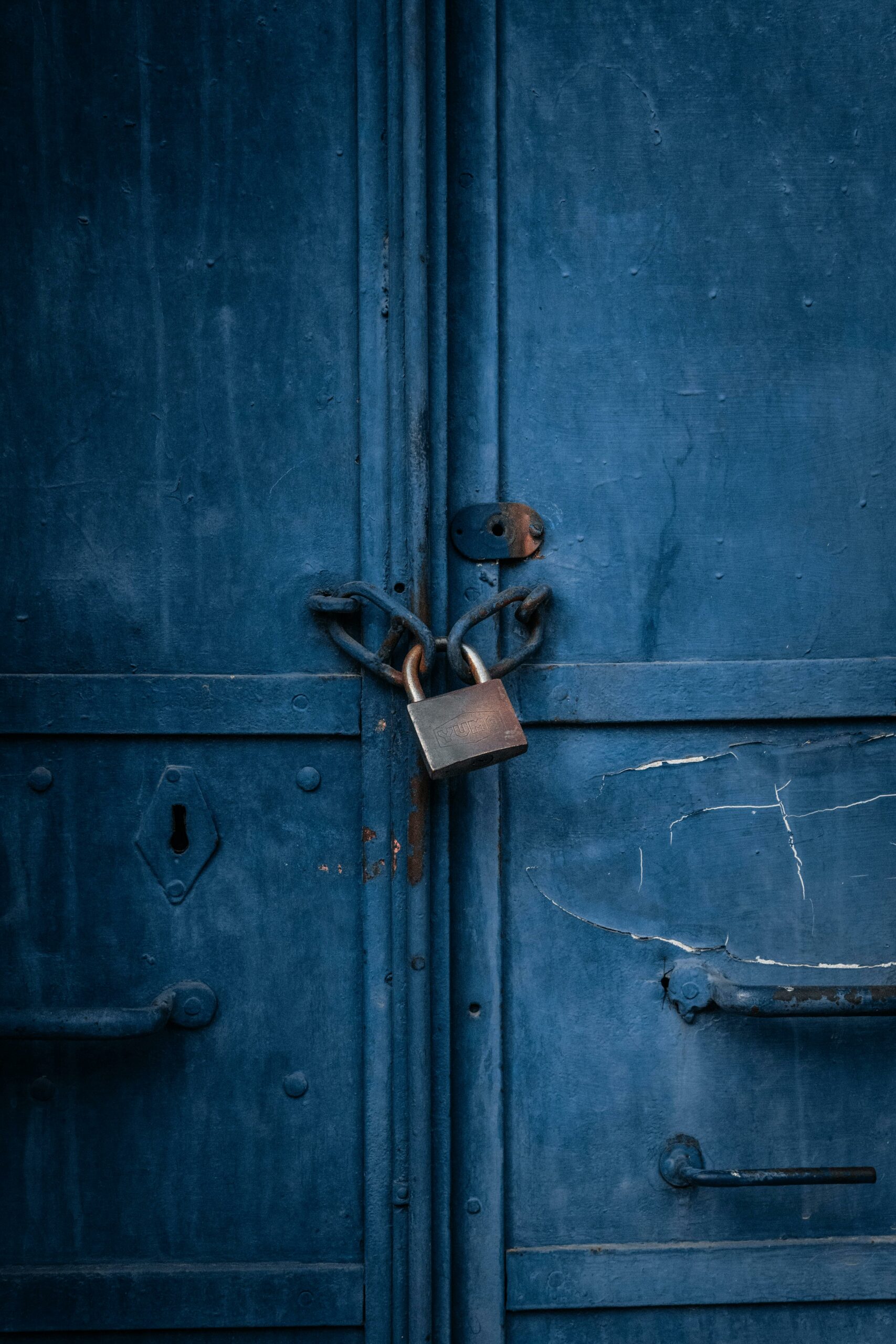 Aged blue door secured with a padlock and chains — photo by Ltf0graphy on Pexels