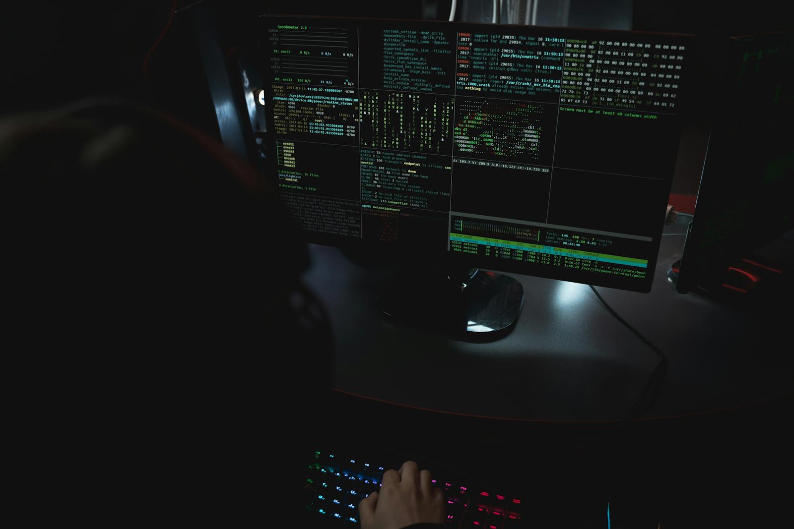 Person at a desk with multiple monitors showing code in a dark room — photo by Tima Miroshnichenko on Pexels