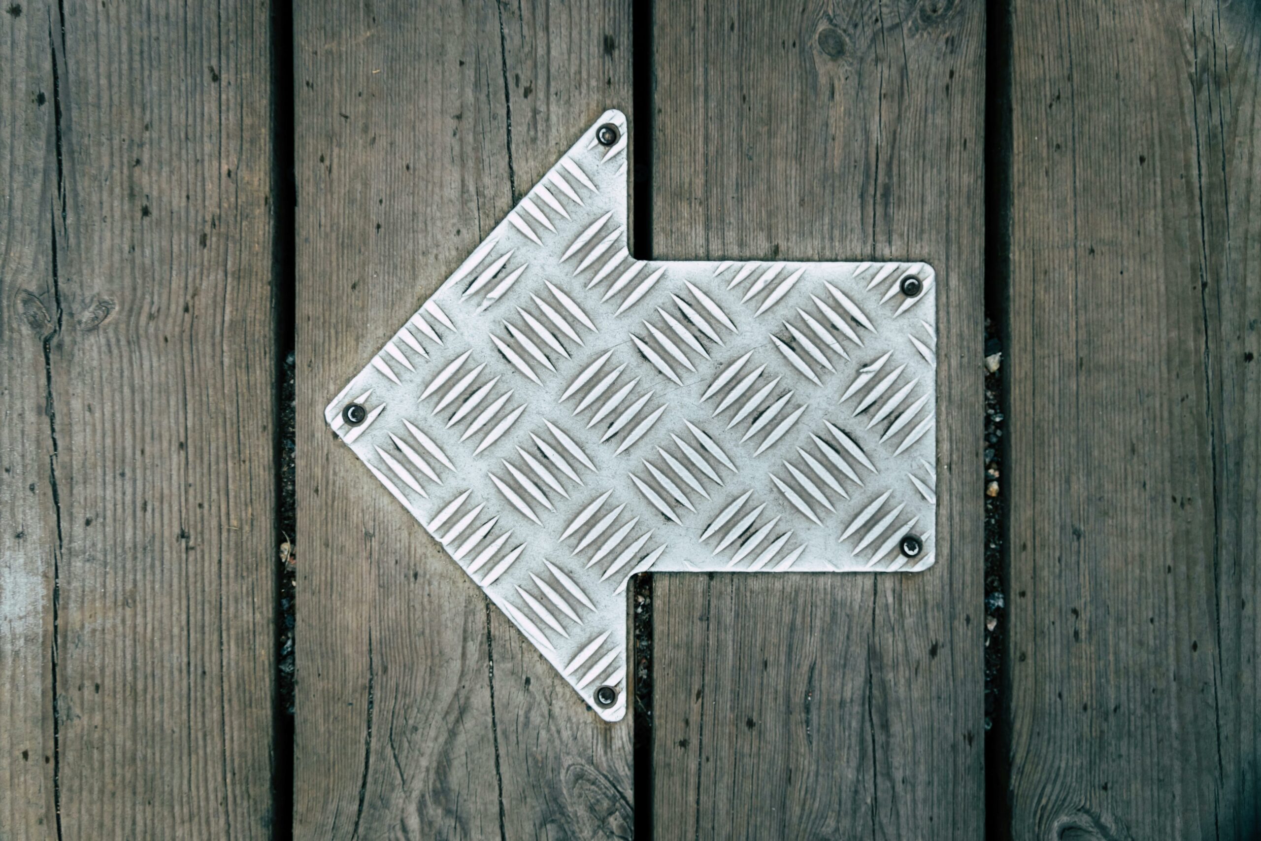 Metal directional arrow plate on a wooden floor — photo by Max Laurell on Pexels