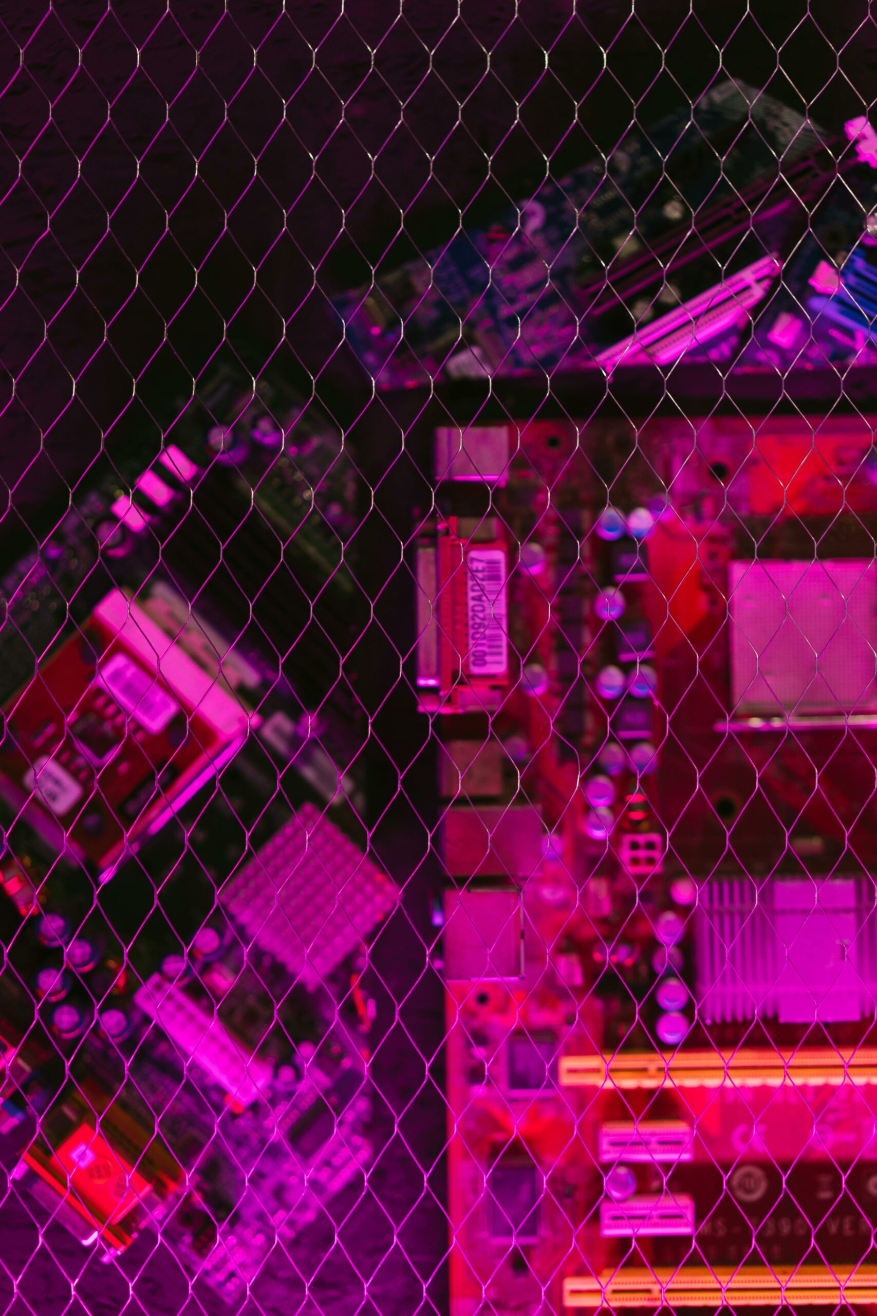 Computer motherboard seen through a wire mesh in pink and purple light — photo by Mikhail Nilov on Pexels